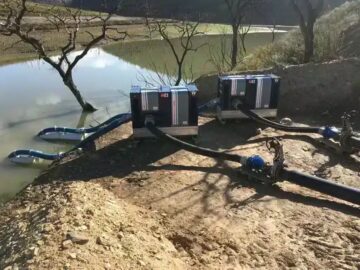 Twee pompsets aan de oever van een waterbassin, met zuigslangen op drijvers in het water en persslangen naar een leiding
